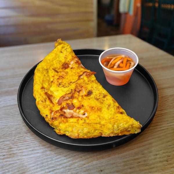A golden-brown Vietnamese bánh xèo pancake with shrimp and pork, served with pickled vegetables.