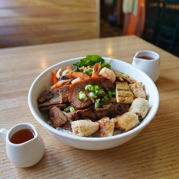 A large bowl of Vietnamese vermicelli noodles with grilled pork, shrimp, spring rolls, and vegetables.